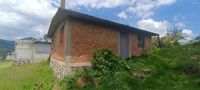 Cabaña de una planta dentro del terreno en venta, rodeada de flores y árboles.